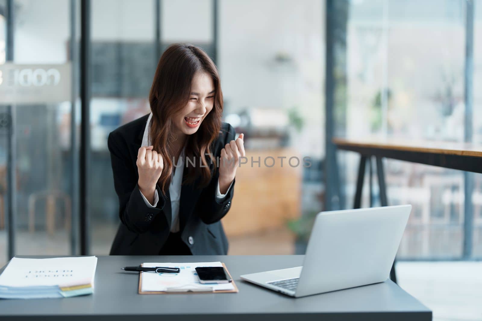 Portrait of a woman business owner showing a happy smiling face as he has successfully invested her business using computers and financial budget documents at work by Manastrong