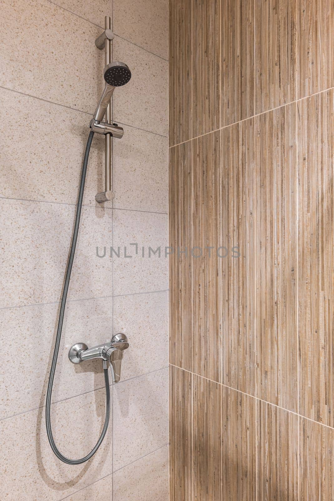 Closeup of a shower area with marble tiles on the walls and metall faucet with a long hose and a shower head. by apavlin