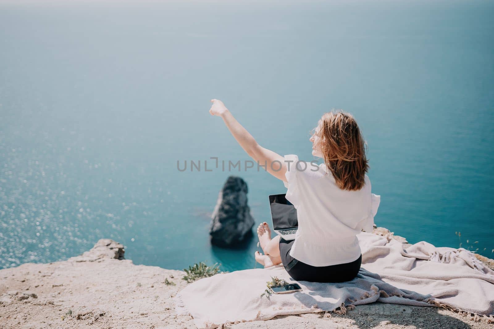 Successful business woman in yellow hat working on laptop by the sea. Pretty lady typing on computer at summer day outdoors. Freelance, travel and holidays concept.