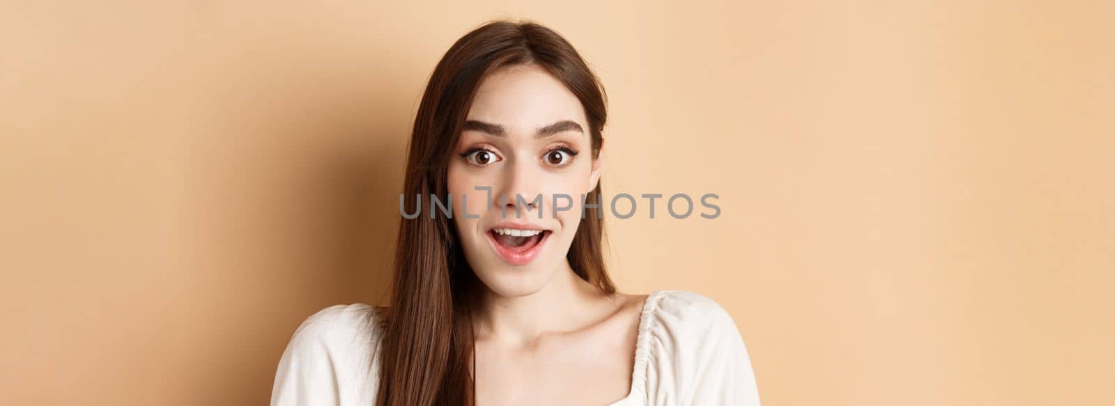 Excited young woman gasping amazed, saying wow and looking at camera, checking out promo offer, standing on beige background by Benzoix