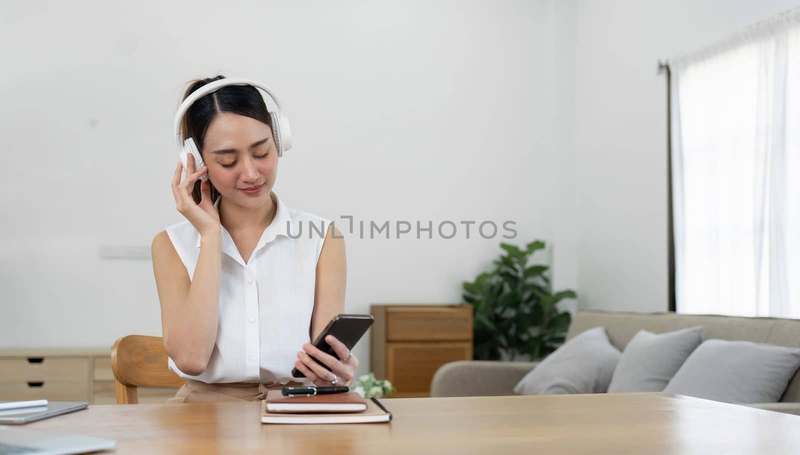 Asian woman listening music with smartphone and wireless headphones at her home. by nateemee