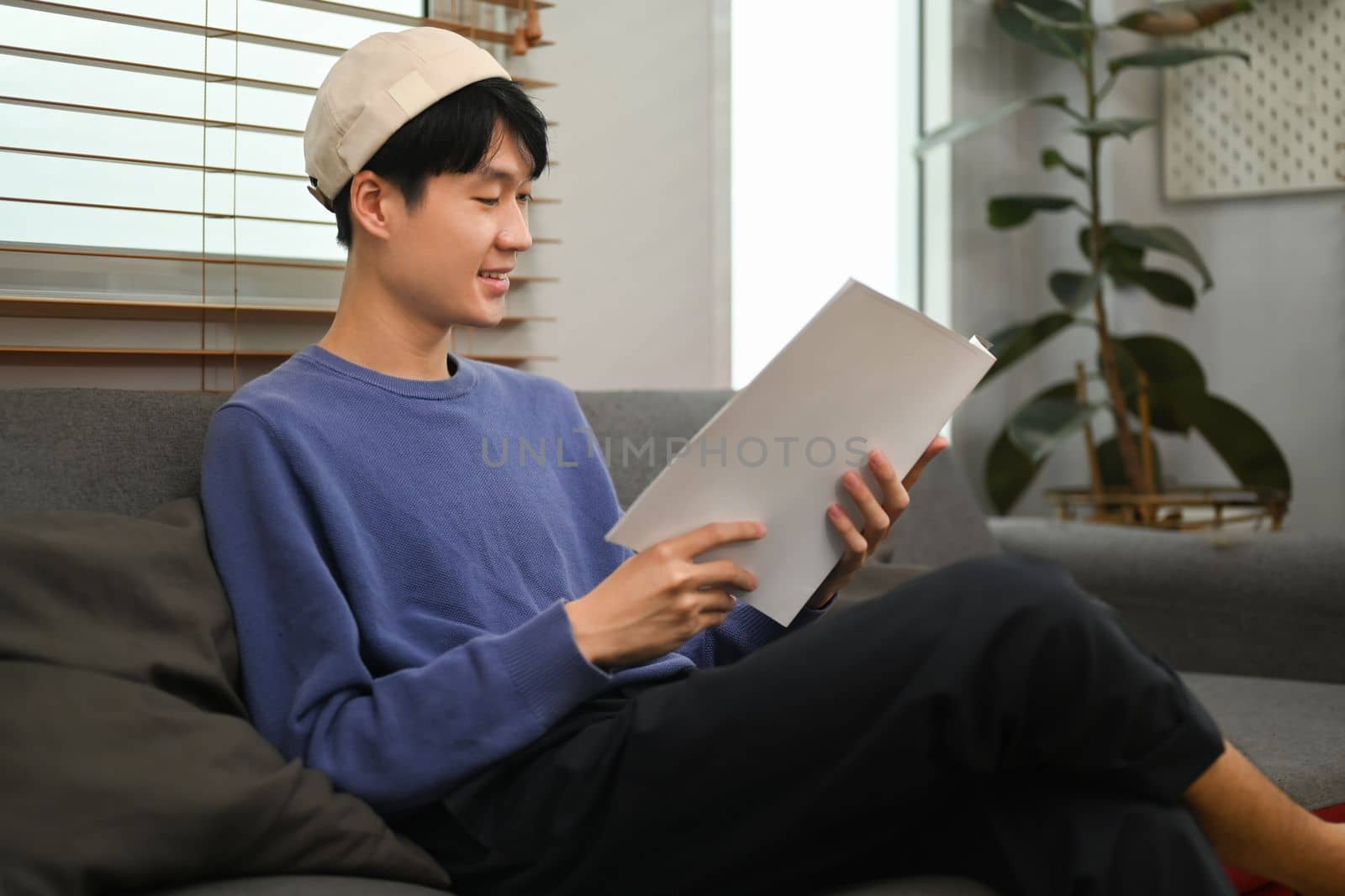 Pleasant man in stylish outfit enjoying reading new novel, relaxing on couch at home.