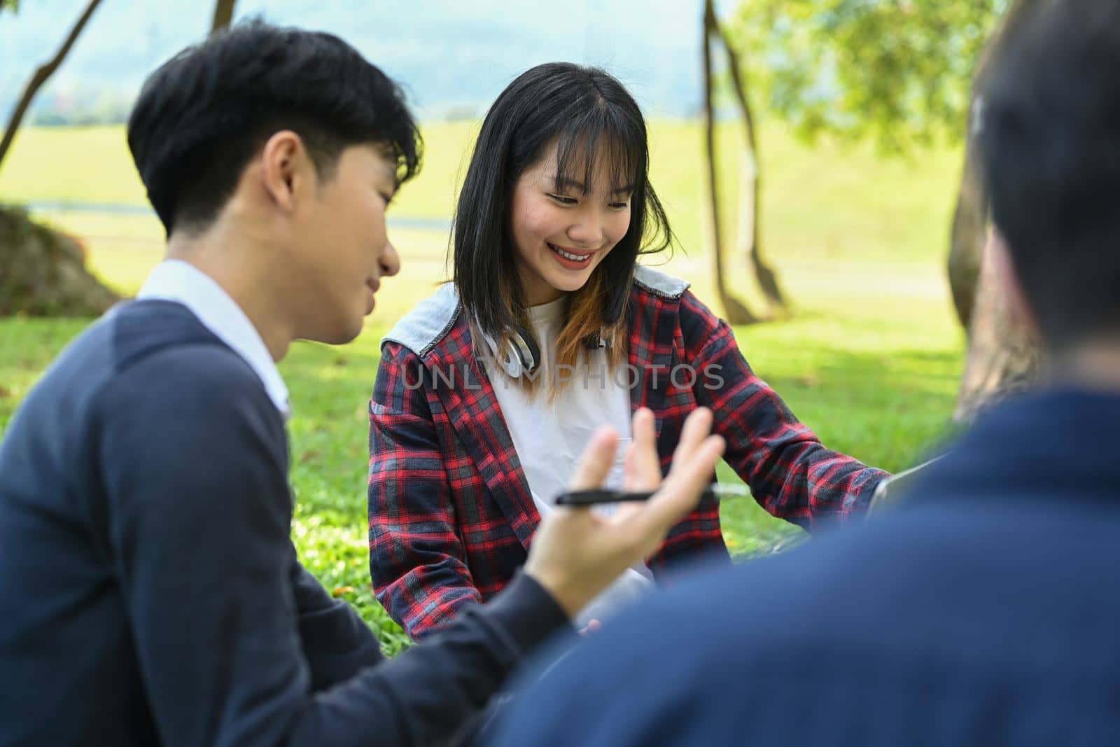 Group of students sitting on grass learning and preparing homework for school lessons. Youth lifestyle and education concept.