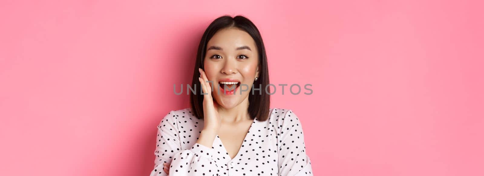 Close-up of beautiful asian woman calling for you, making announcement or yelling, standing over pink background.