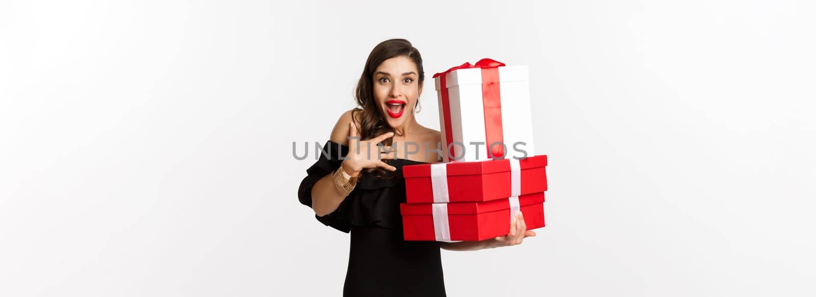 Celebration and christmas holidays concept. Excited and happy woman receive gifts, holding xmas presents and rejoicing, standing in black dress over white background.
