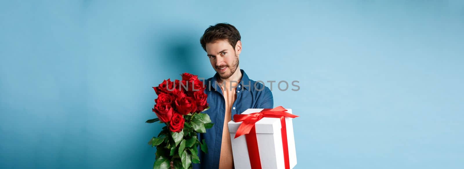 Love and Valentines day concept. Romantic man giving you gift box and bouquet of flowers on date, standing over blue background.