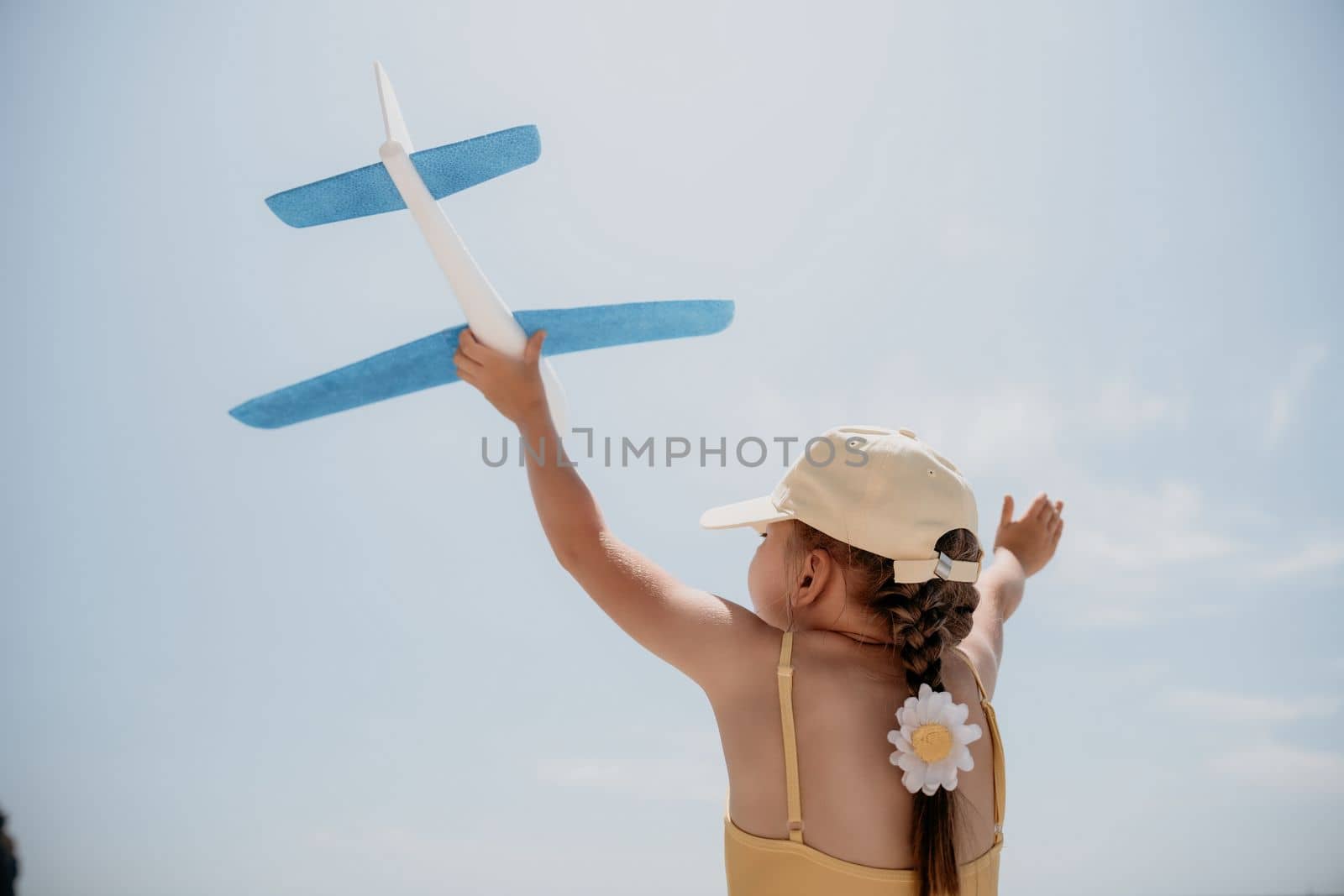 Kid playing with toy airplane. Children dream of travel by plane. Happy child girl has fun in summer vacation by sea and mountains. Outdoors activities at background of blue sky. Lifestyle moment
