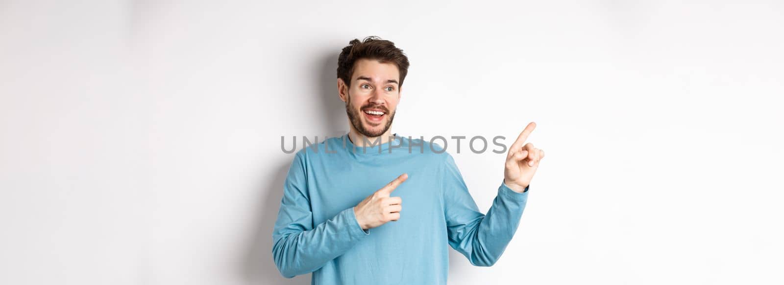 Excited bearded man checking out special offer, pointing and looking at advertisement with happy face, standing over white background.