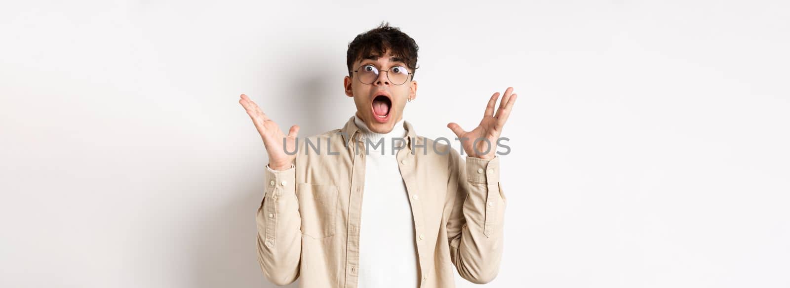 Scared young man in panic, screaming and looking axious, jumping startled and shocked, shaking hands nervously, standing on white background by Benzoix