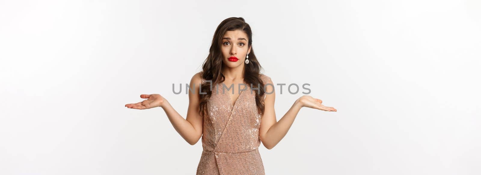 Concept of casino, celebration and party. Confused beautiful woman in glamour dress looking indecisive, shrugging clueless, standing over white background.