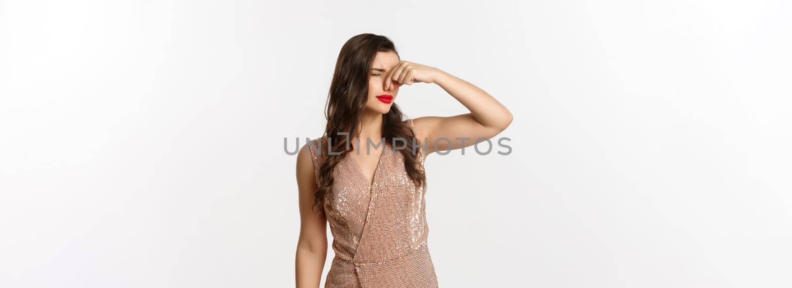 Attractive young woman with red lips, glamour dress, shut nose with fingers from disgusting smell, something reek, standing over white background.