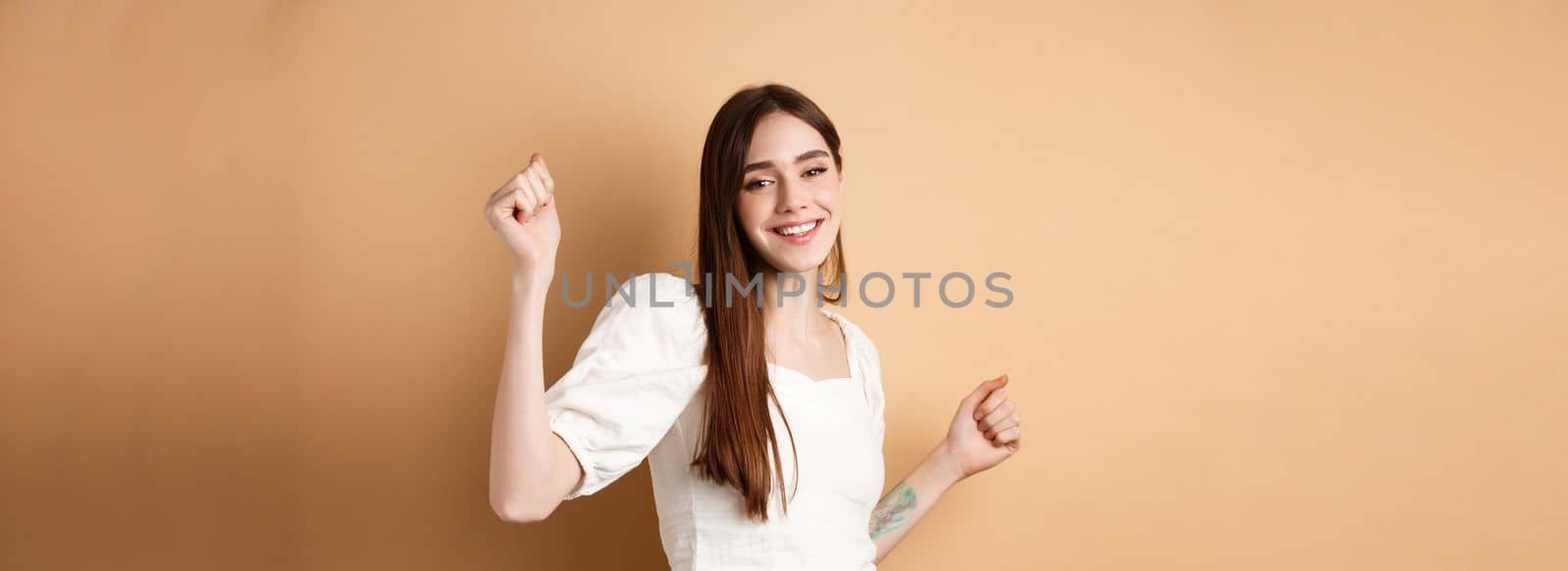 Happy woman dancing and having fun, close eyes and smiling, standing on beige background.