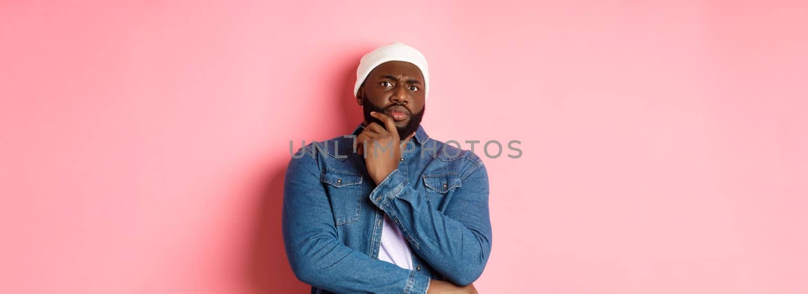 Doubtful african american man staring at camera with disbelief, standing skeptical and thinking, pink background.