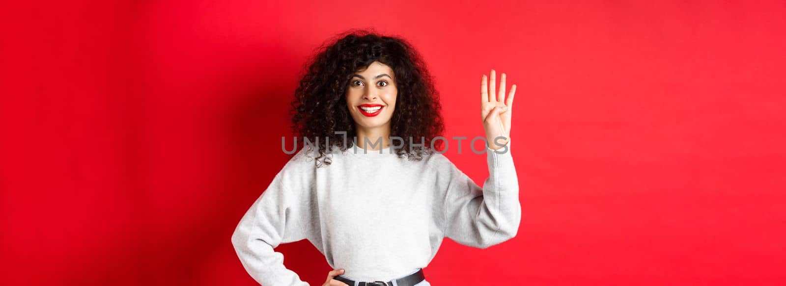 Excited woman with curly hair showing number four with fingers, making order, standing against red background by Benzoix