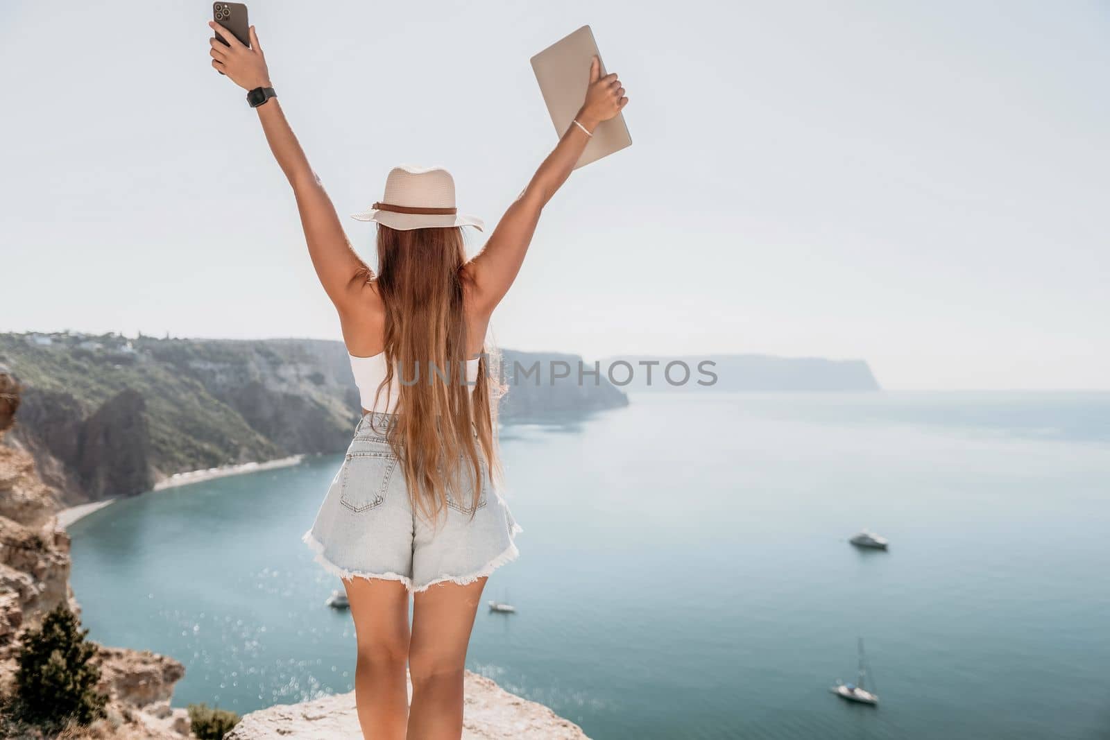 Woman sea laptop. Business woman in yellow hat freelancer with laptop working over blue sea beach. Girl relieves stress from work. Freelance, digital nomad, travel and holidays concept by panophotograph