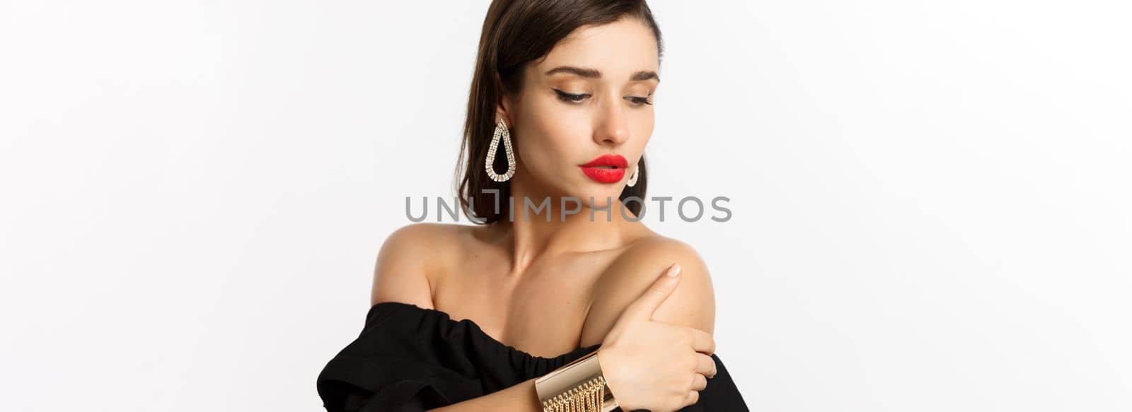 Fashion and beauty concept. Elegant woman with red lips, black dress, showing earrings and jewelry, white background by Benzoix