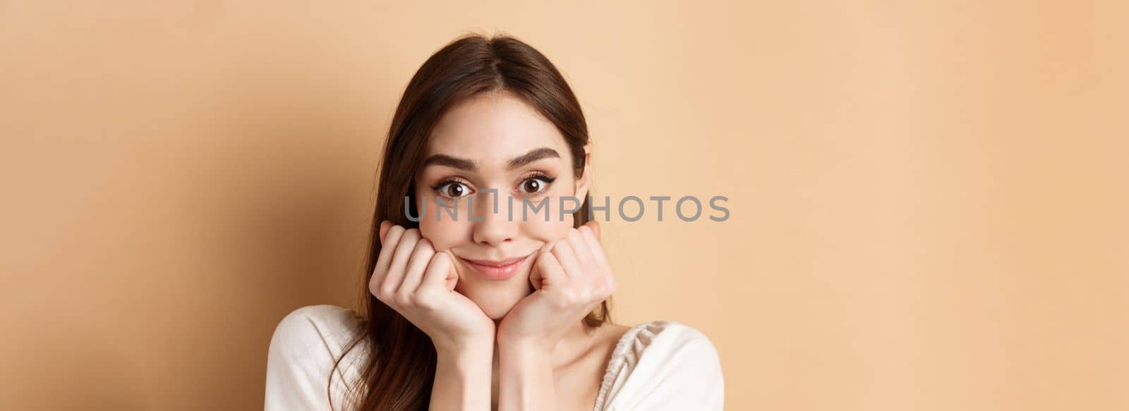 Portrait of intrigued girl listening with interest and excitement, hear interesting story, smiling amused, standing on beige background by Benzoix