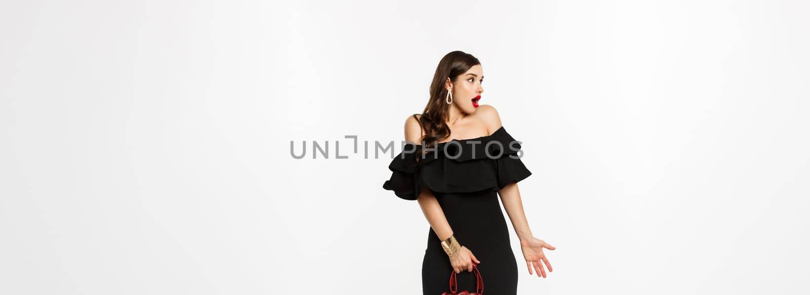Beauty and fashion concept. Full length of surprised woman in elegant dress, heels looking left confused, holding purse, cant understand what happening, white background.