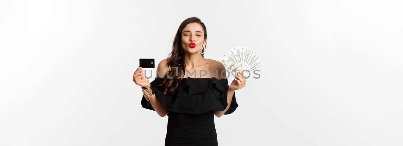 Beauty and shopping concept. Pretty glamour woman pucker lips for kiss, showing credit card and dollars, standing over white background.