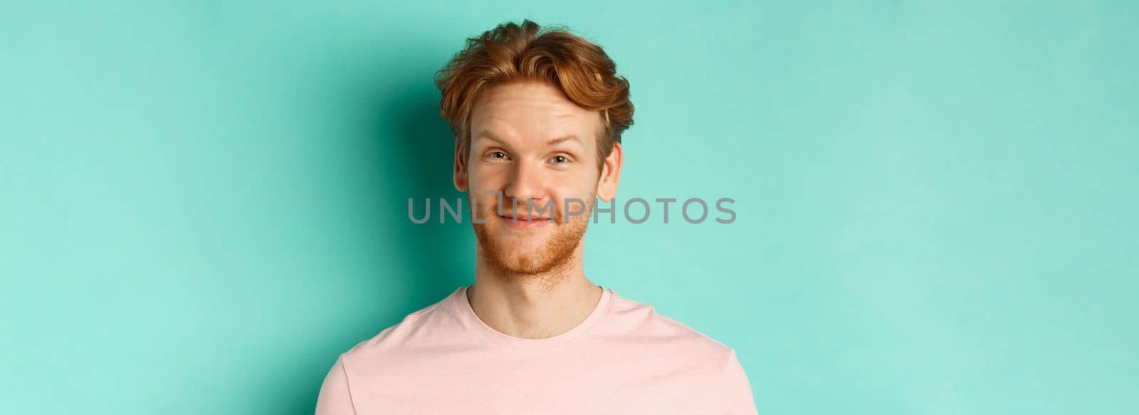 Close up of redhead bearded man looking pleased, nod in approval and smiling, standing in pink t-shirt against turquoise background by Benzoix