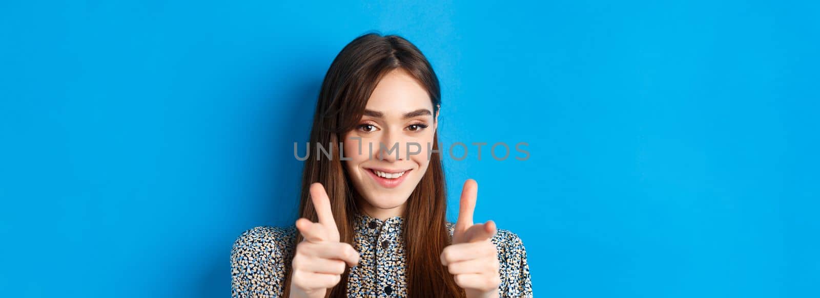 Excited and confident beauty woman, pointing fingers at camera and smiling, invite and beckon you, join us gesture, praising good choice, standing on blue background.