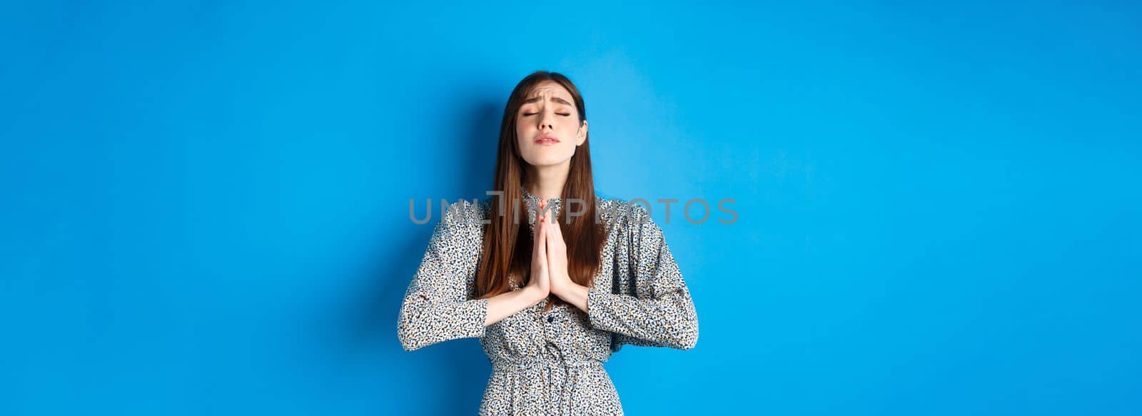 Pleading woman in dress begging for wish come true, supplicating god, standing against blue background by Benzoix