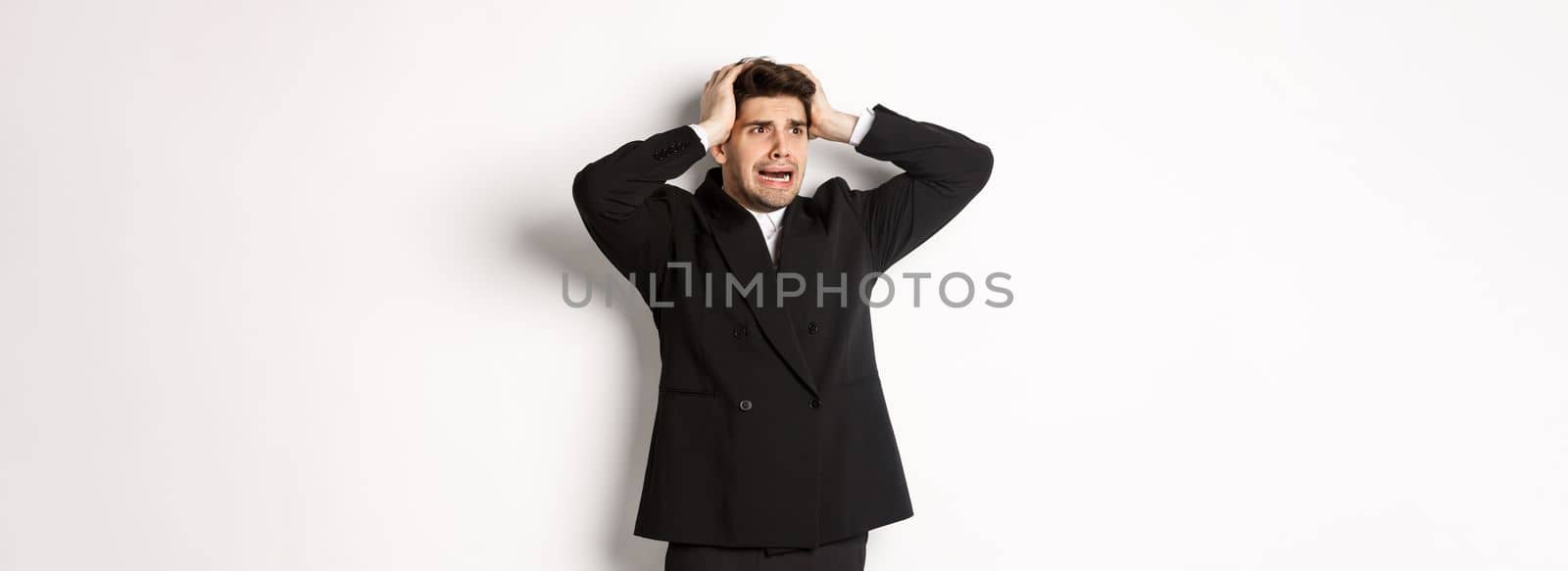 Image of anxious businessman start to panic, looking left with worried expression, standing in black suit over white background by Benzoix