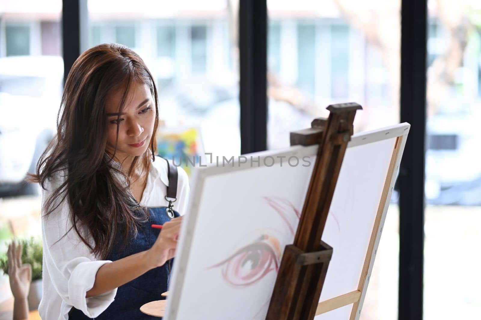 Attractive woman painting picture on canvas at her creative workplace.