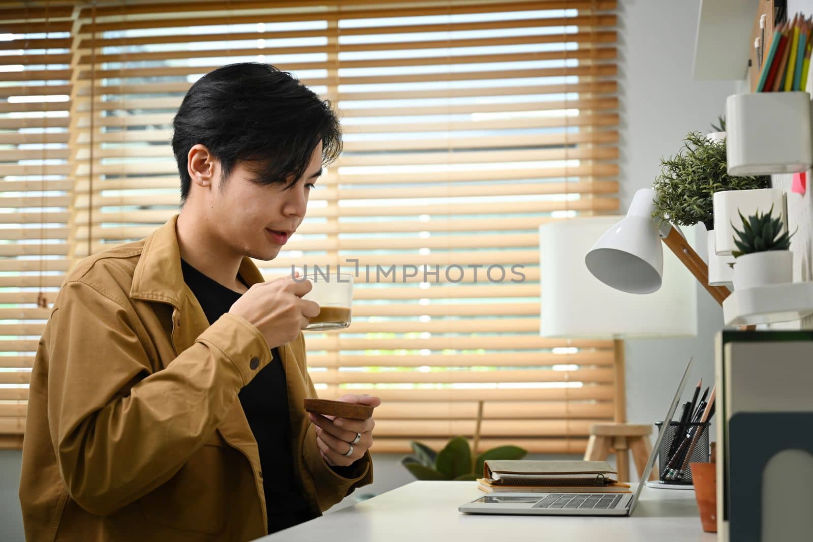 Young Asian man drinking coffee and reading email on laptop computer. by prathanchorruangsak
