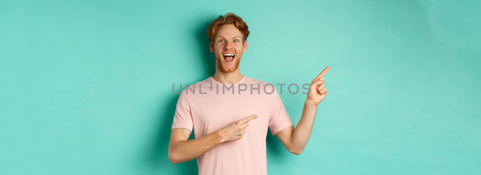 Cheerful caucasian man in t-shirt looking happy, pointing fingers left and showing promo offer, standing over turquoise background.