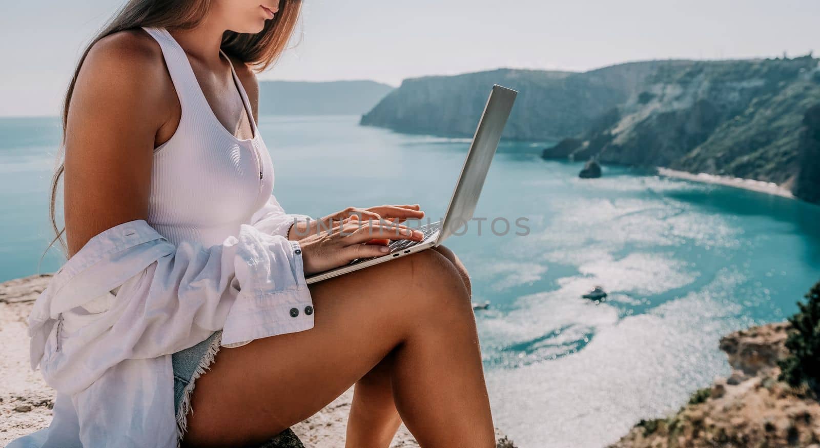 Digital nomad, Business woman working on laptop by the sea. Pretty lady typing on computer by the sea at sunset, makes a business transaction online from a distance. Freelance remote work on vacation