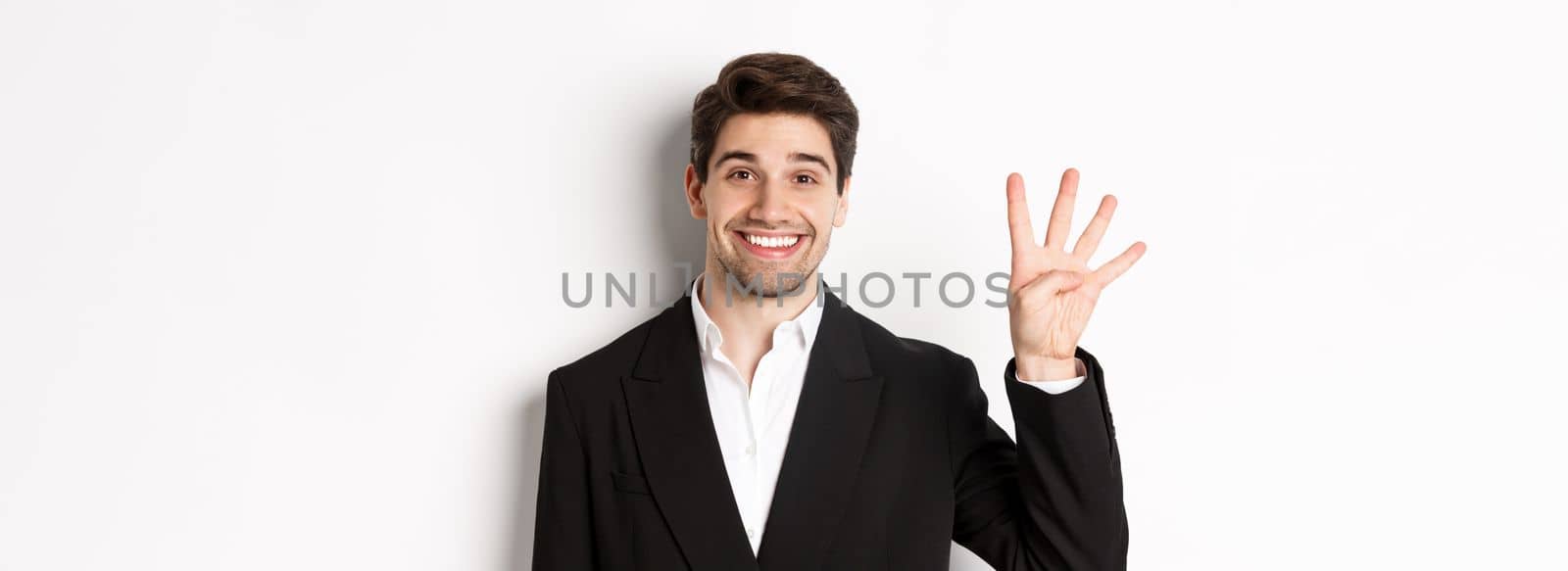 Close-up of handsome businessman in black suit, smiling amazed, showing number four, standing over white background by Benzoix