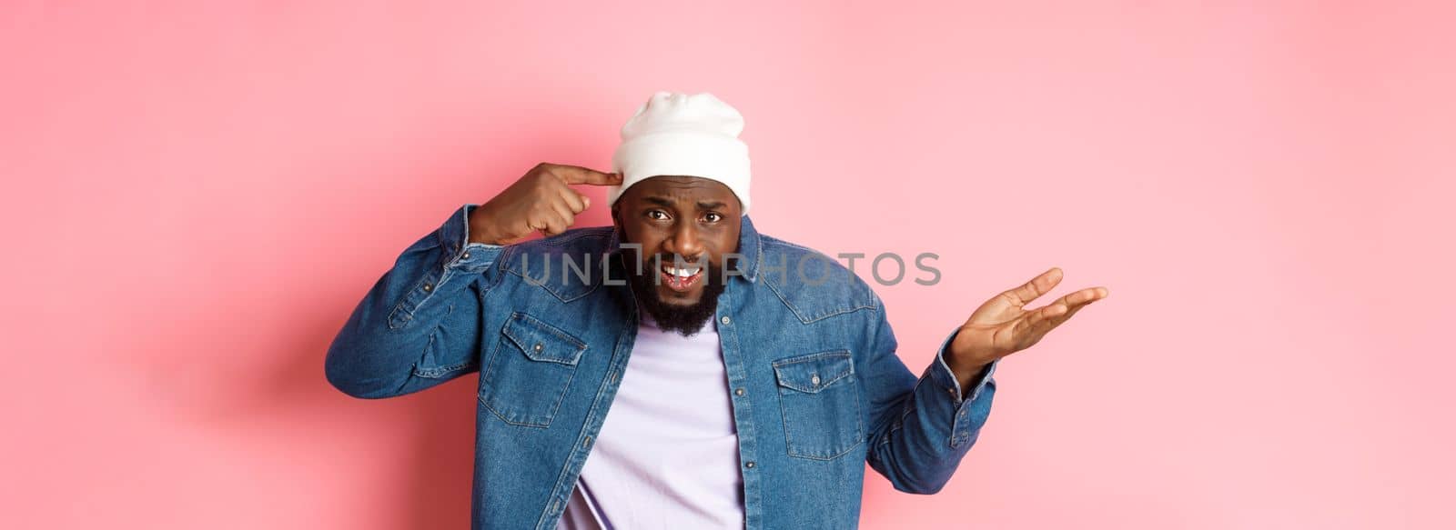 Annoyed and pissed-off african-american man pointing finger at head, scolding someone stupid, staring bothered at camera, pink background by Benzoix