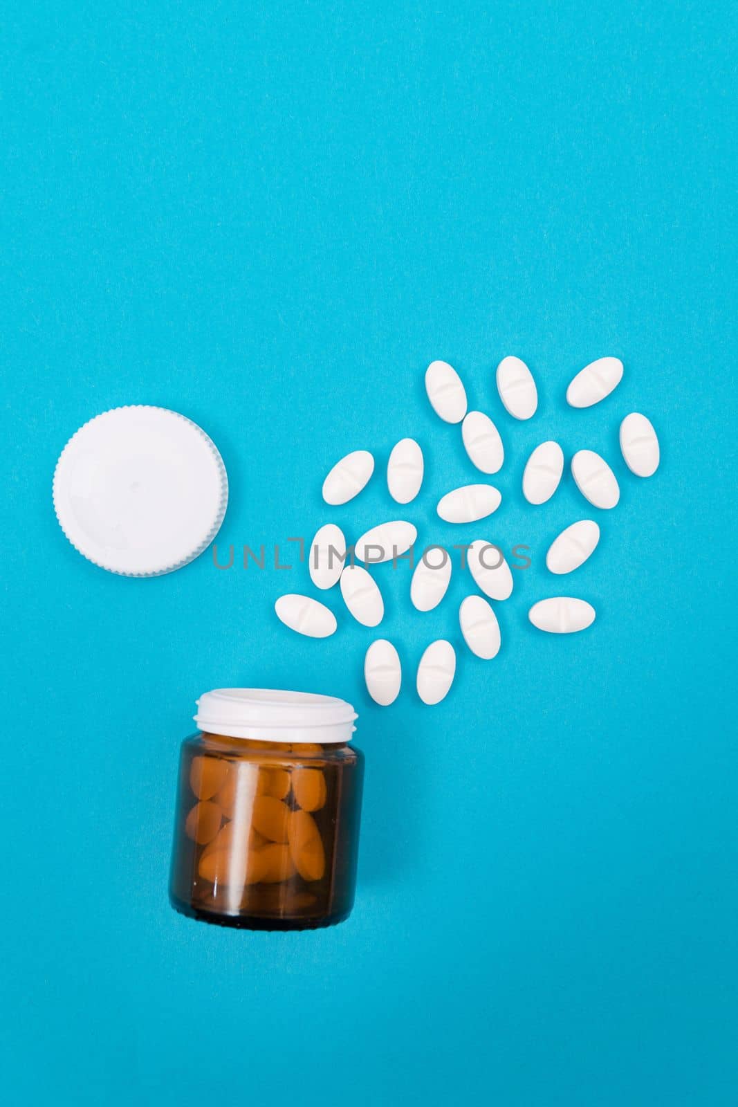 Global Pharmaceutical Industry and Medicinal Products - White Pills or Tablets Scattered from the Pill Container, Lying on Blue Background