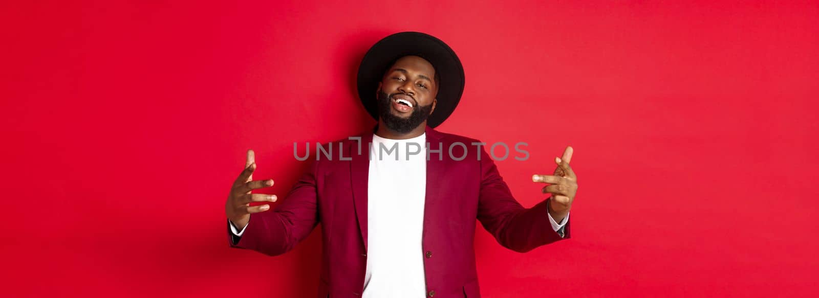 Christmas shopping and people concept. Confident and sassy man showing bring it on gesture, dancing hip hop and looking self-assured at camera, red background.