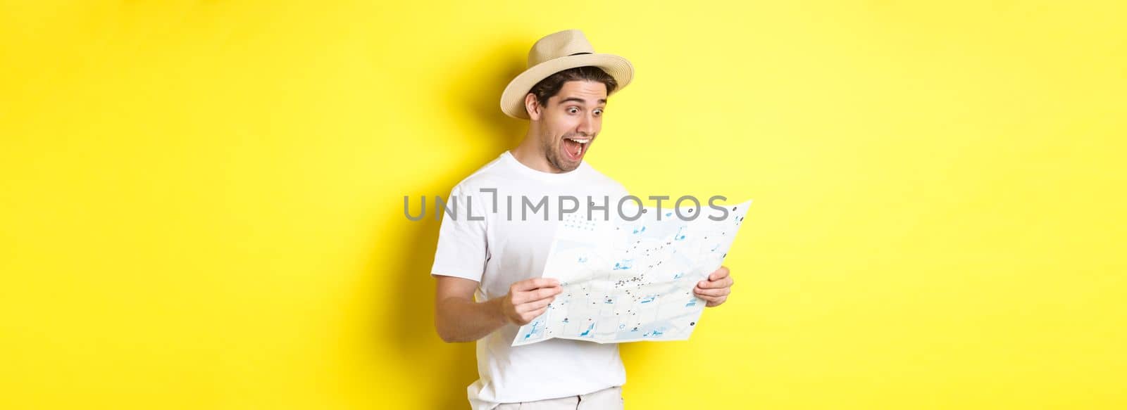 Travelling, vacation and tourism concept. Smiling happy tourist looking at map with sightseeings, standing against yellow background.
