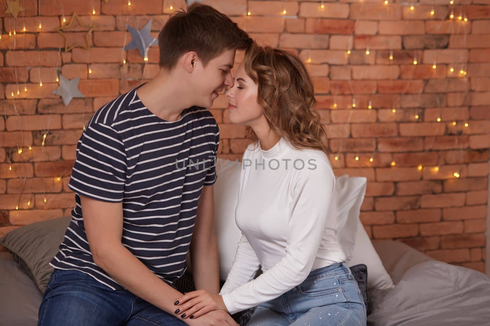 Happy loving couple relaxing on bed at home, young man touching smiling beautiful woman face, looking in the eyes enjoying togetherness and tenderness in love, close up view