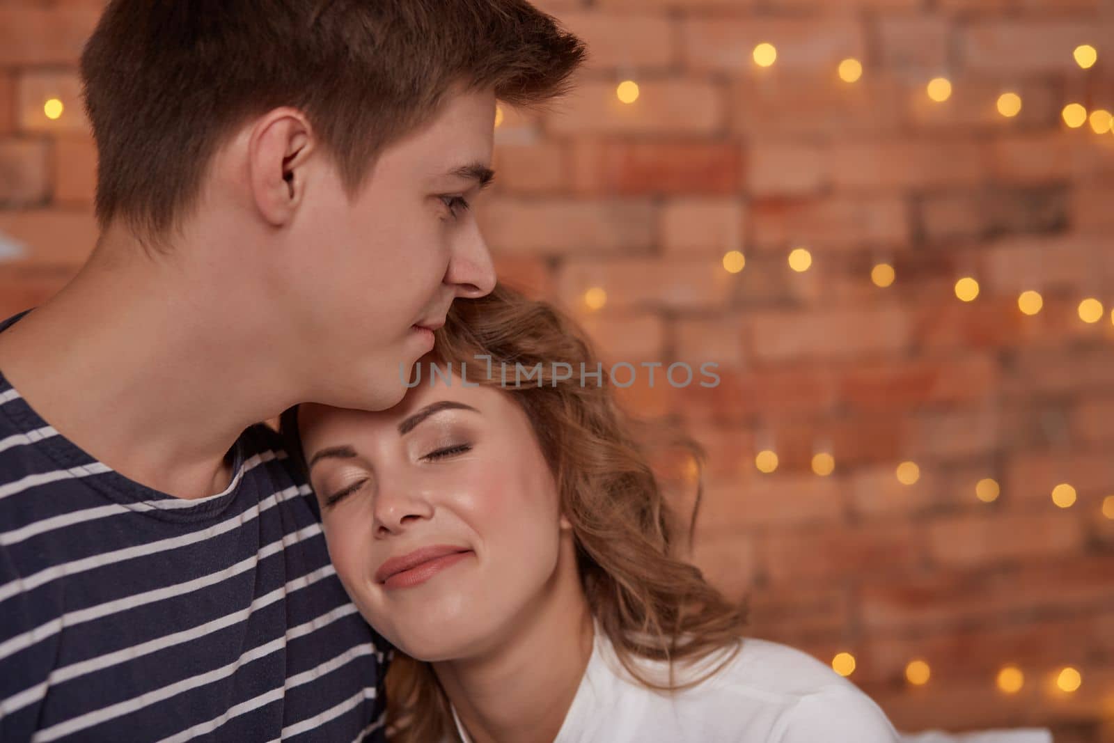 Relation emotions. Young man embracing attractive brunette wife indoor. They are in love and happy