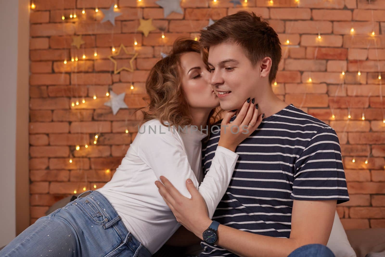 Happy loving couple relaxing on bed at home, young woman touching smiling handsome man face, looking in the eyes. enjoying togetherness and tenderness in love, close up view