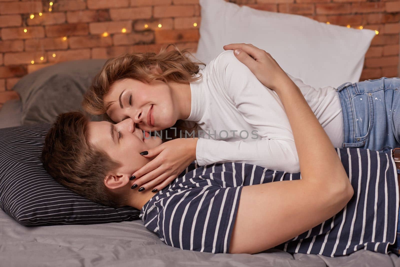 Caucasian young beautiful couple lie on bed and hugging each other. They look each other in the eyes and they are happy