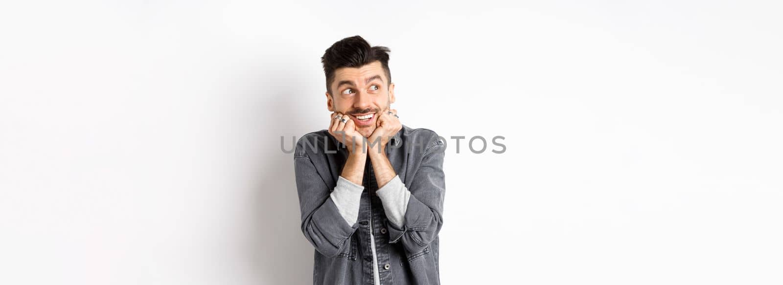 Excited cute young man look dreamy at upper left corner, waiting for parcel, daydreaming or imaging something, standing on white background.