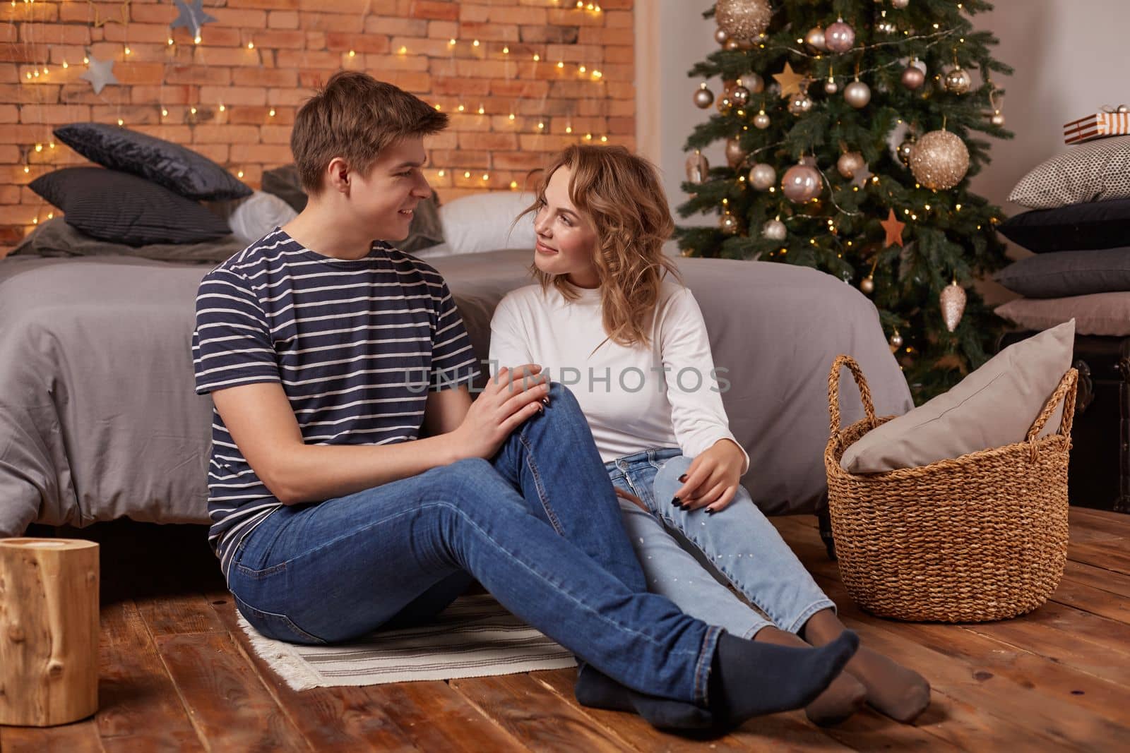 Close up portrait of a beautiful couple sitting on the floor embracing and looking to each other. They are in love and happy