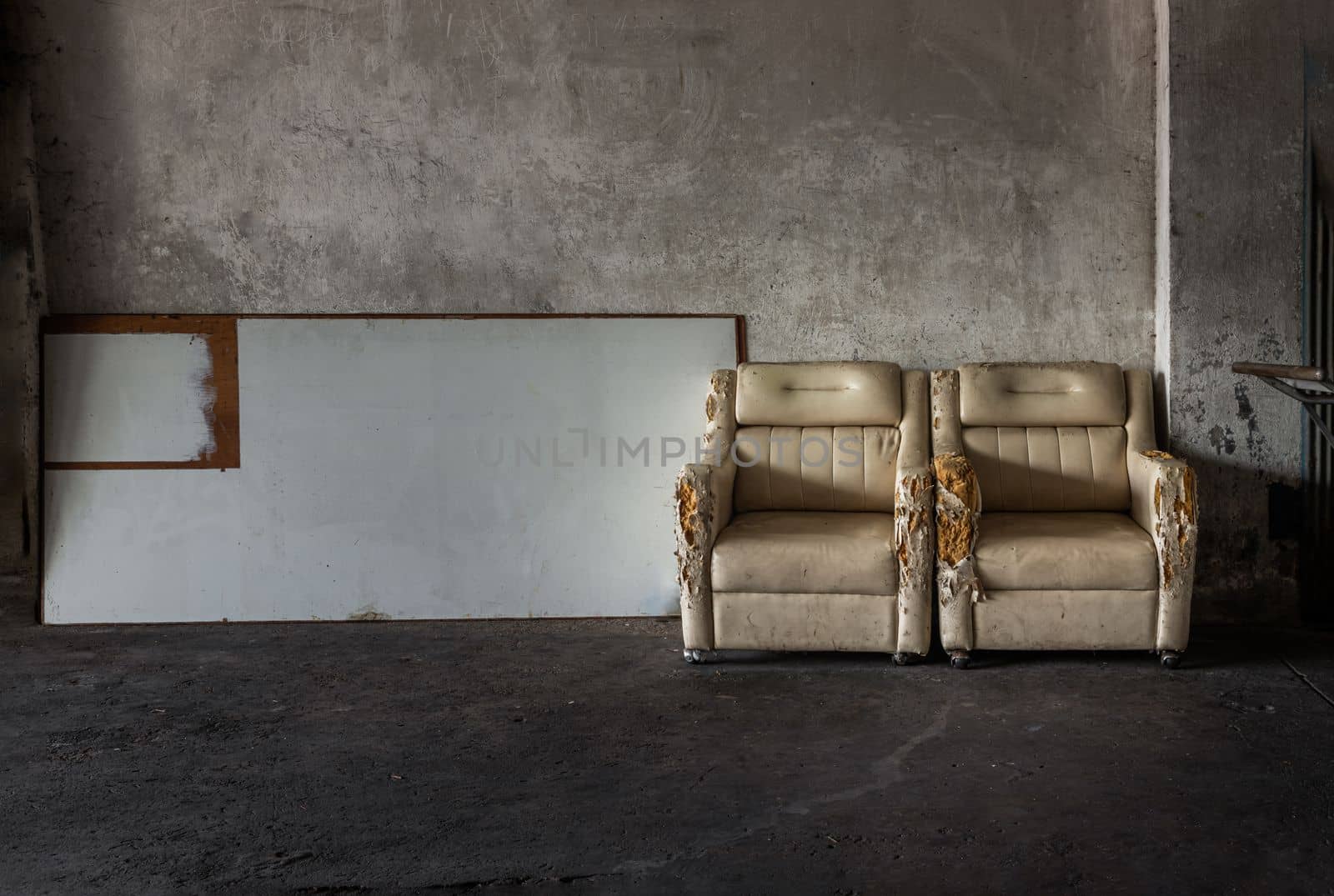 Two old white upholstered armchairs and white planks in front of cement wall in of an abandoned factory site. Copy space, Selective Focus.