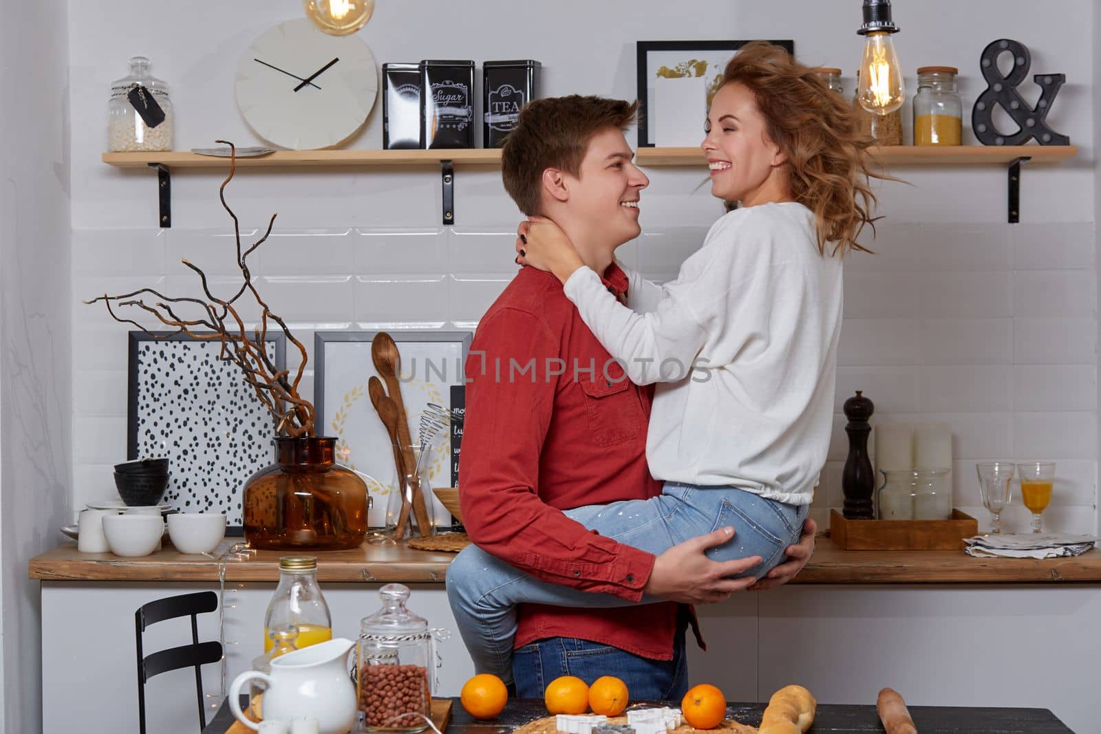 Happy young lovely couple on kitchen hugging each other. They enjoy spending time togehter. The man holding his girlfriend