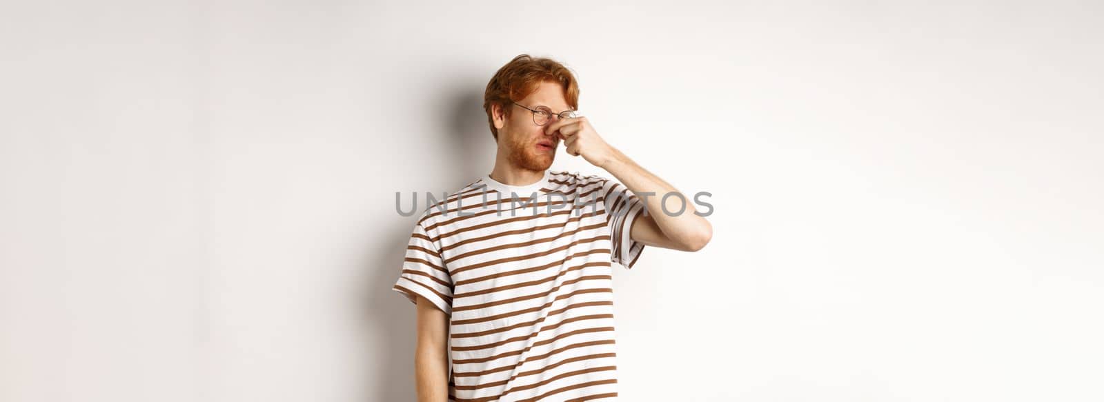 Young man with red hair staring at camera and shut nose from bad smell, looking disgusted as something reek, white background by Benzoix