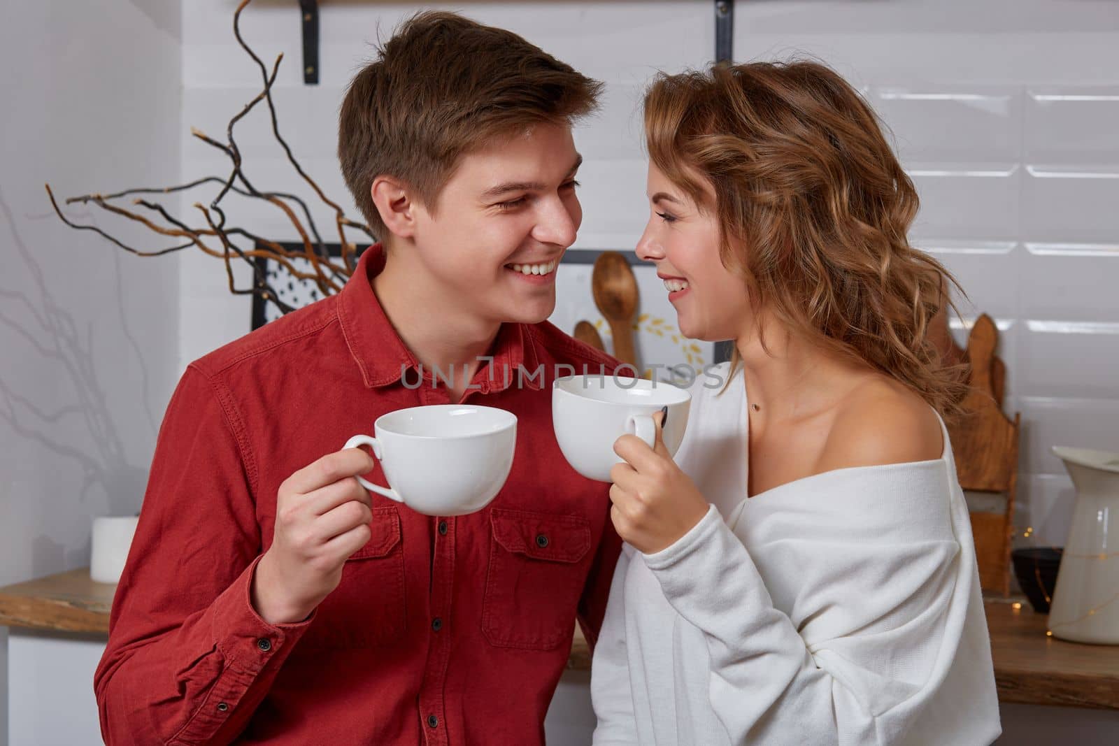 Happy young lovely couple on kitchen hugging each other. They enjoy spending time togehter. They drink coffee and smiling