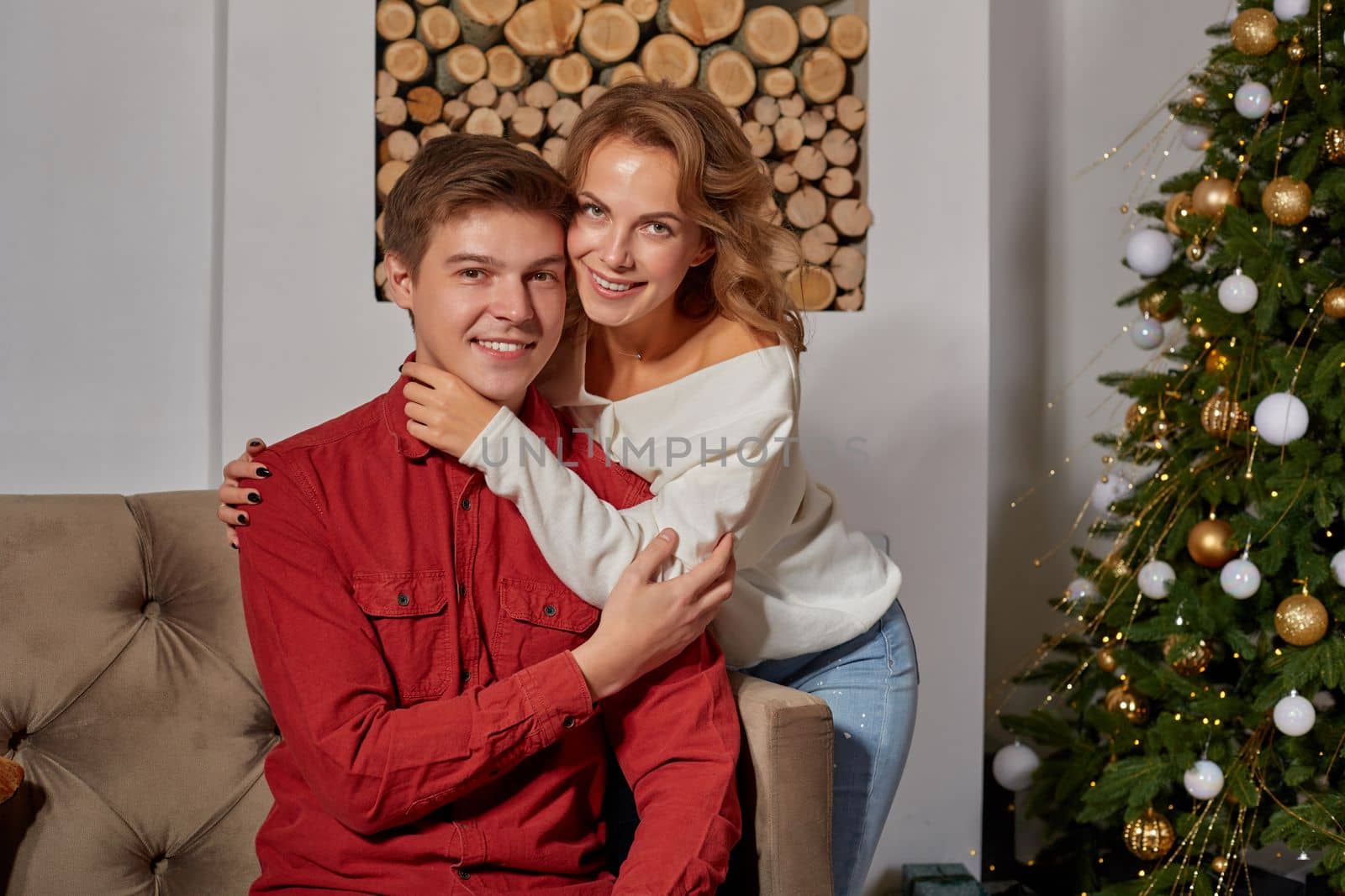 Happy young lovely couple on living room sitting on the couch near christmass tree enjoying each other