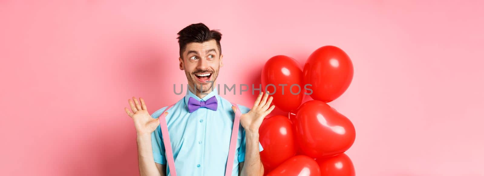 Love and romance concept. Happy man screaming from fantastic news, shouting wow and smiling amused, checking out special offer on Valentines, standing near red hearts balloons.
