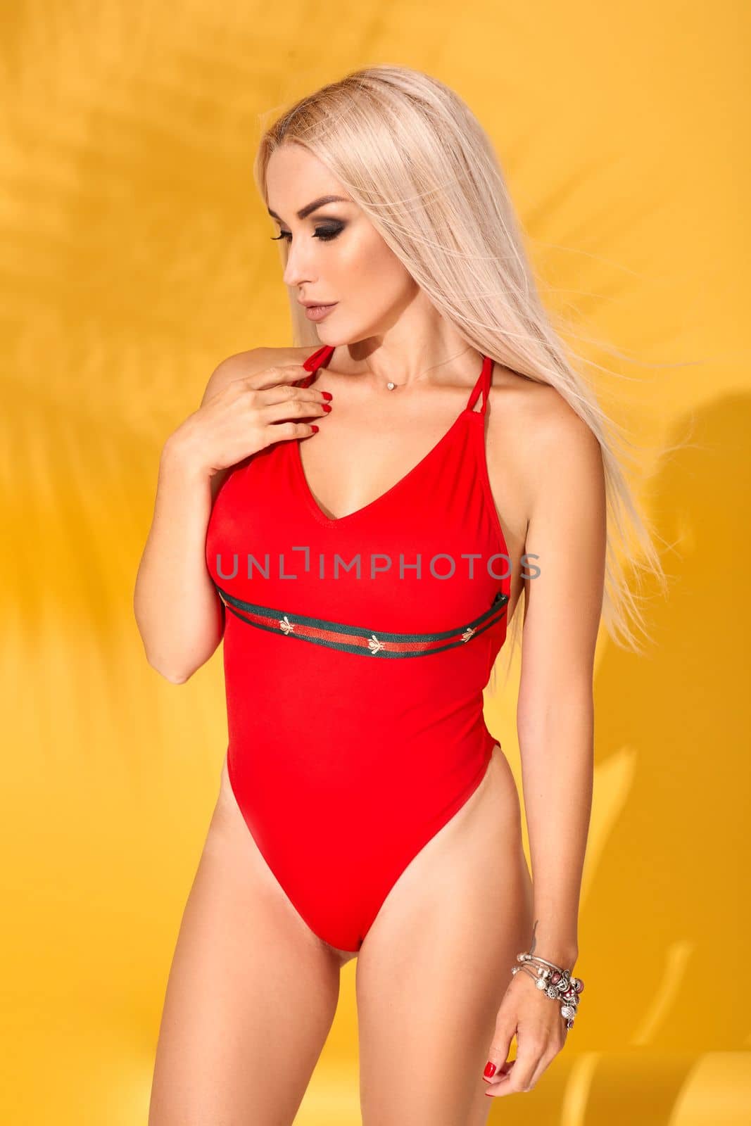 Young sexy blonde woman with long straight hair posing in studio. Perfect gorgeous pale body, red swimsuit or bikini