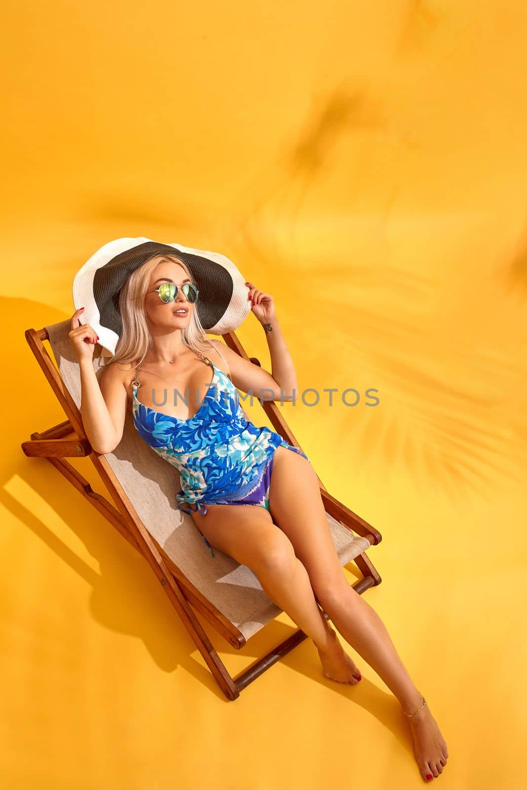 Beautiful young blonde woman in blue swimsuit lies on the lounger on yellow background by nazarovsergey